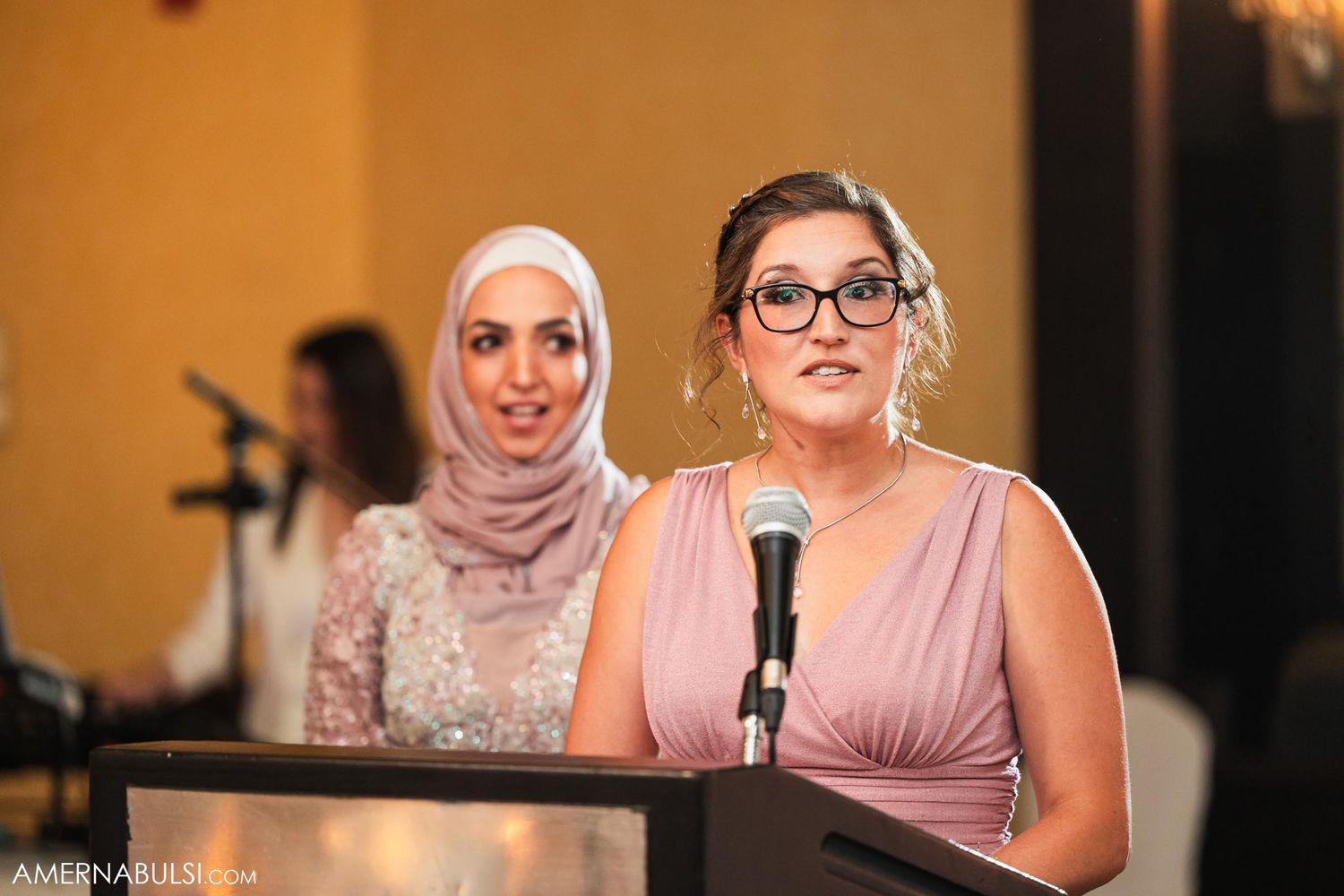 Two wedding guests in formal attire deliver a speech together at an elegant reception venue.