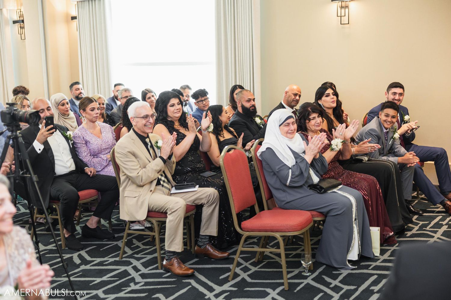 Wedding guests seated in chairs watching ceremony in decorated reception hall.