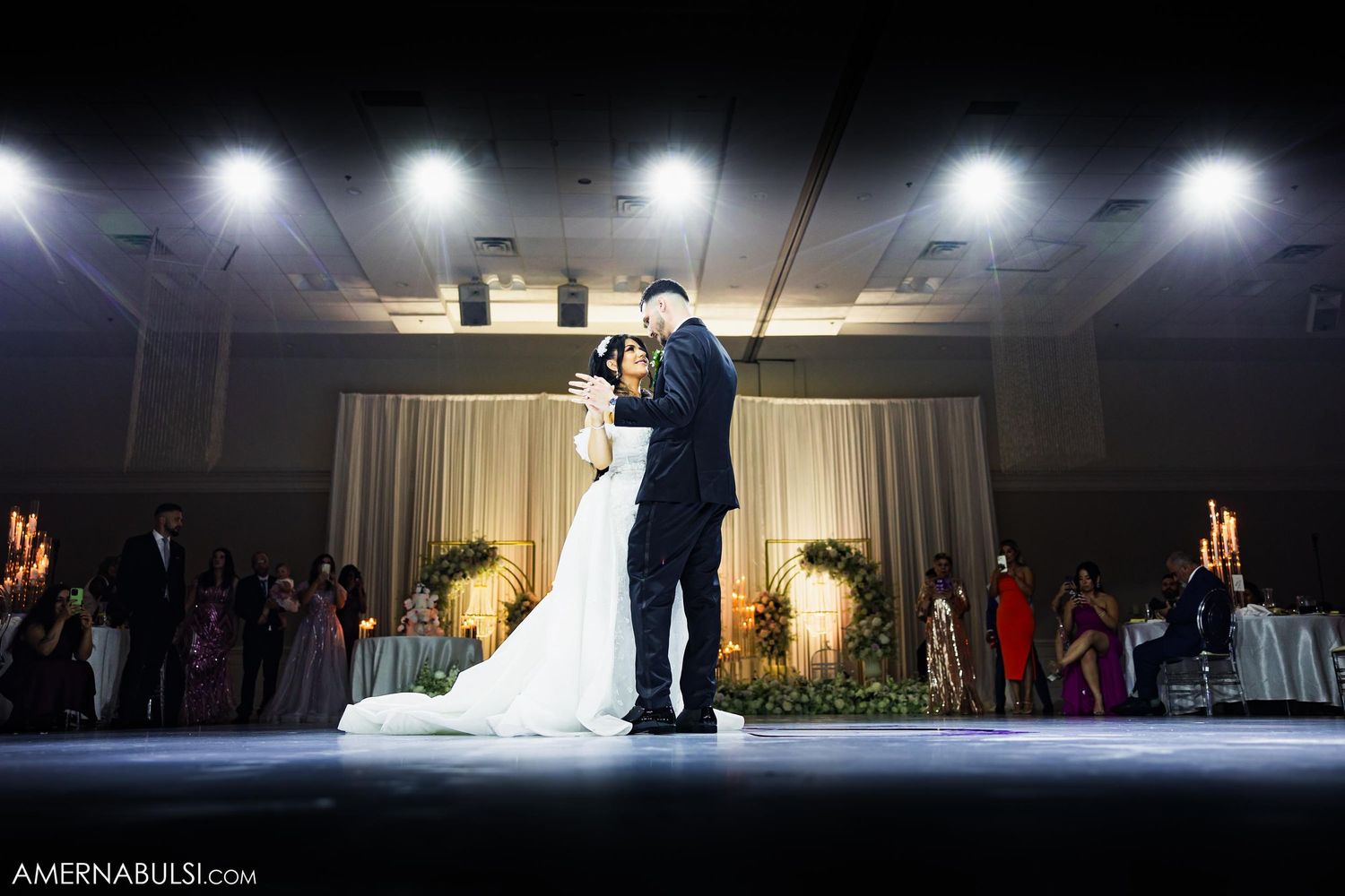 Dramatic spotlit first dance at wedding reception on dark stage.