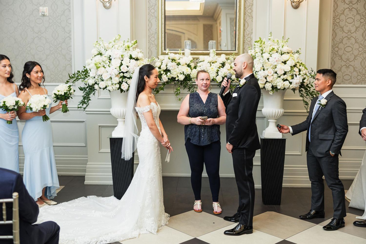 Wedding ceremony in elegant room with white floral arrangements and classic decor.