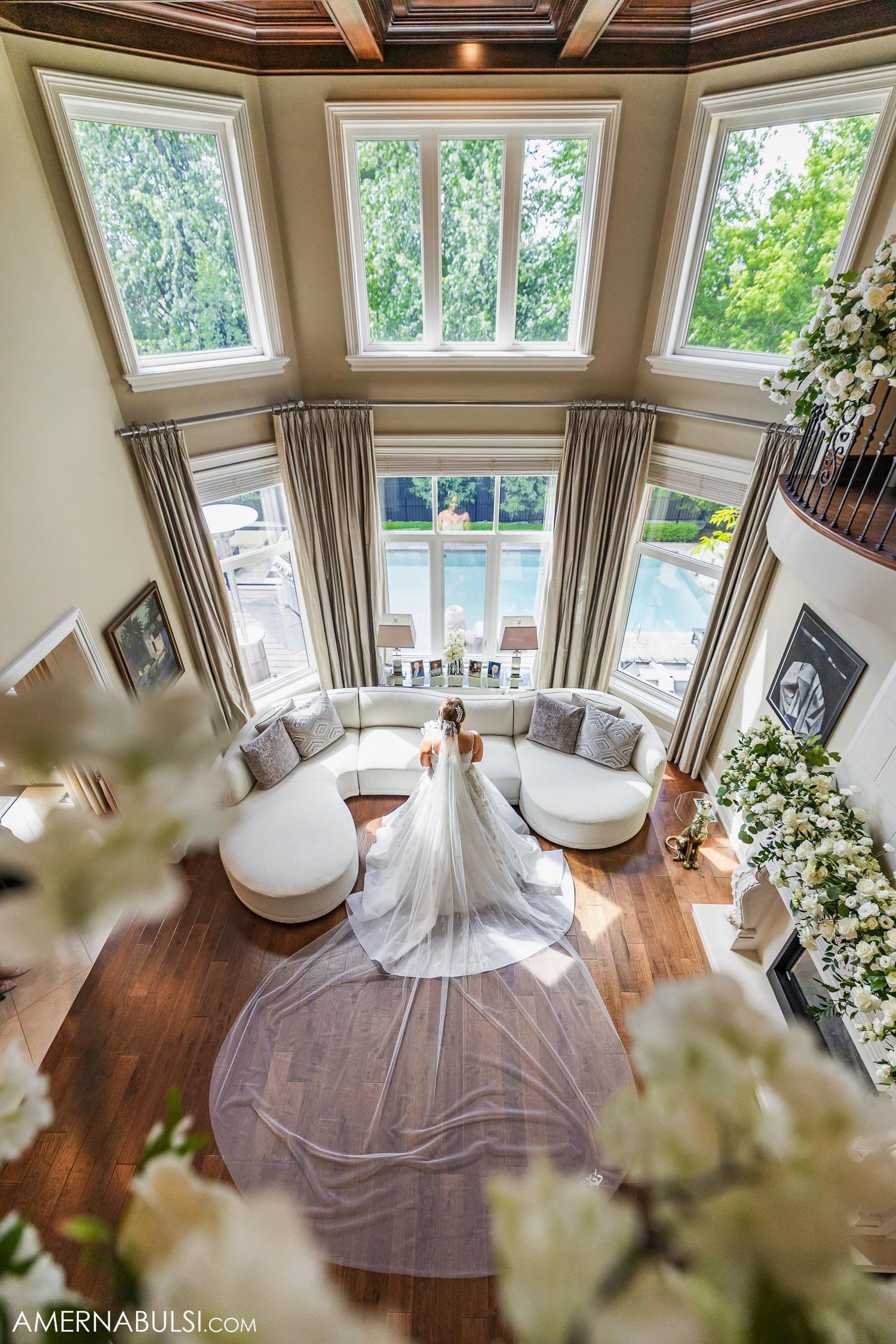 A sweeping wedding dress train fills an elegant living room with tall windows and modern decor.