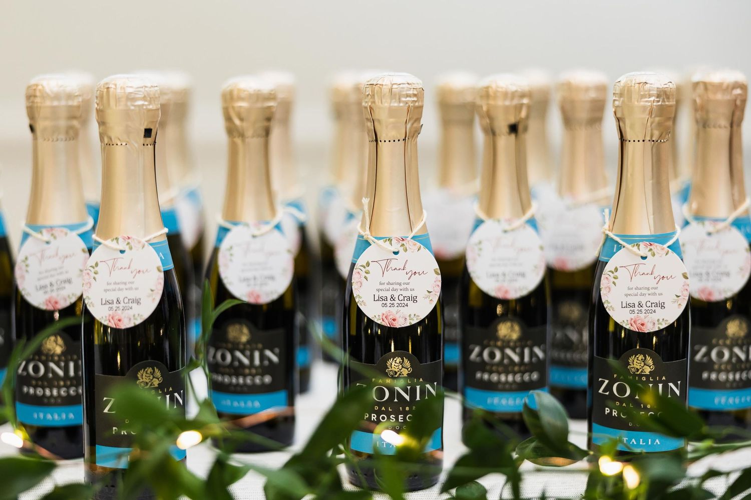 Row of Zonin prosecco bottles with blue tags arranged for wedding favors.