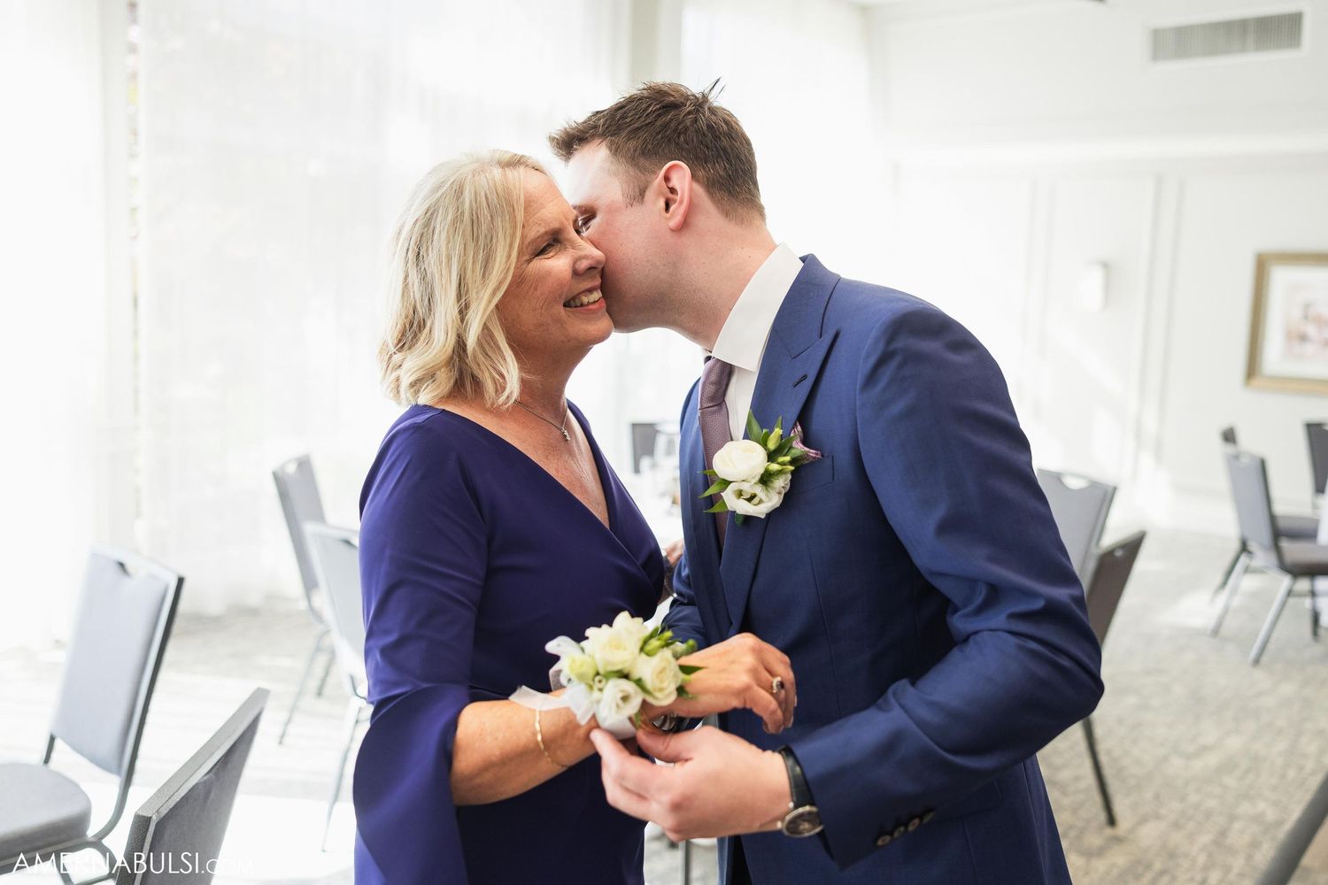 A couple in formal attire share a tender moment while holding boutonniere flowers.