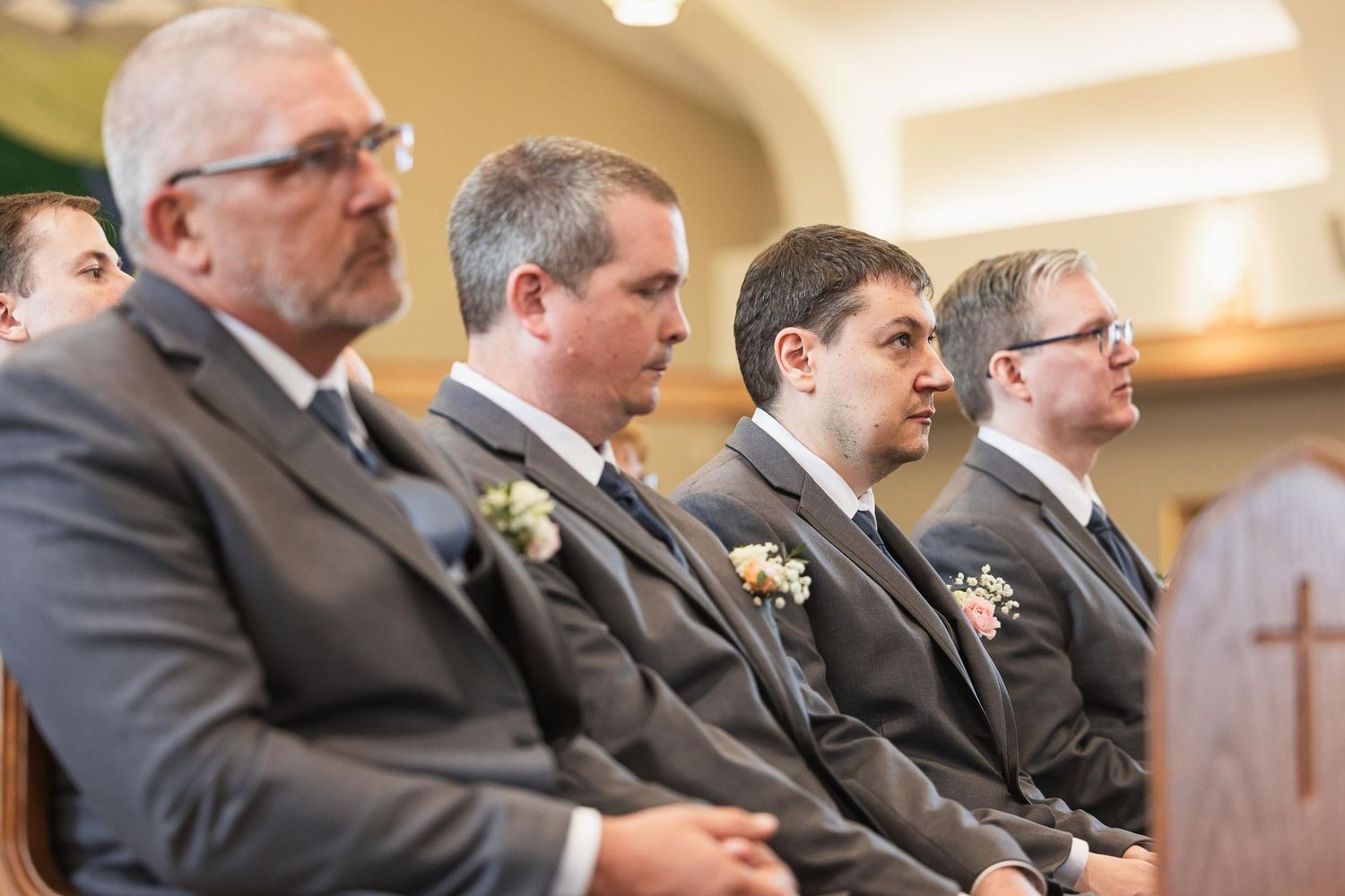 Groomsmen in dark suits sitting attentively during wedding ceremony.
