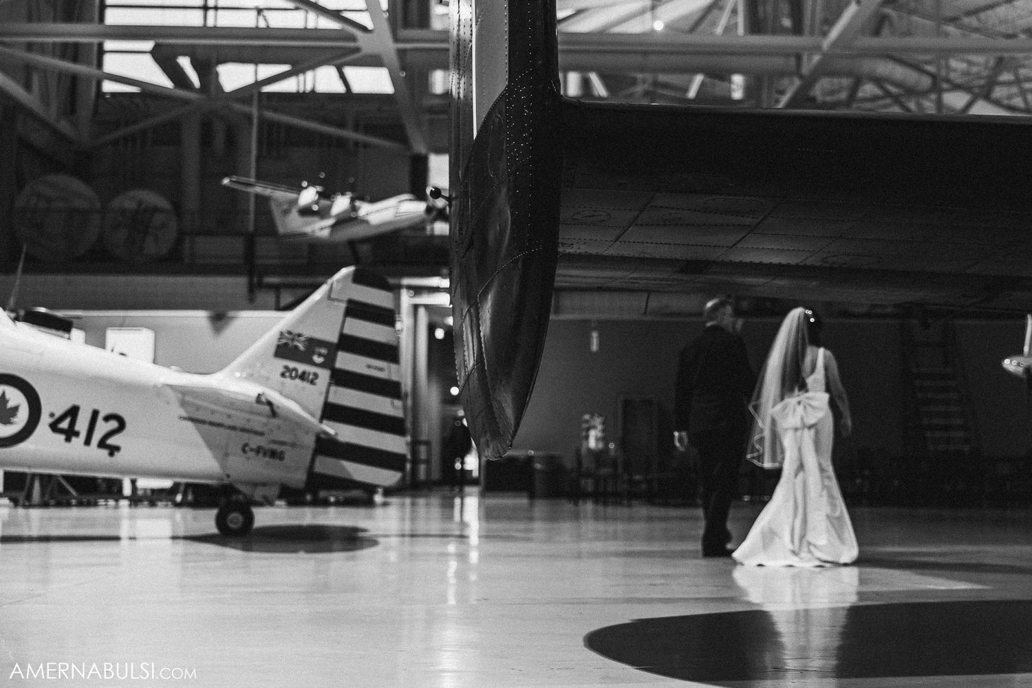 Dramatic black and white wedding photo with vintage aircraft in hangar background.