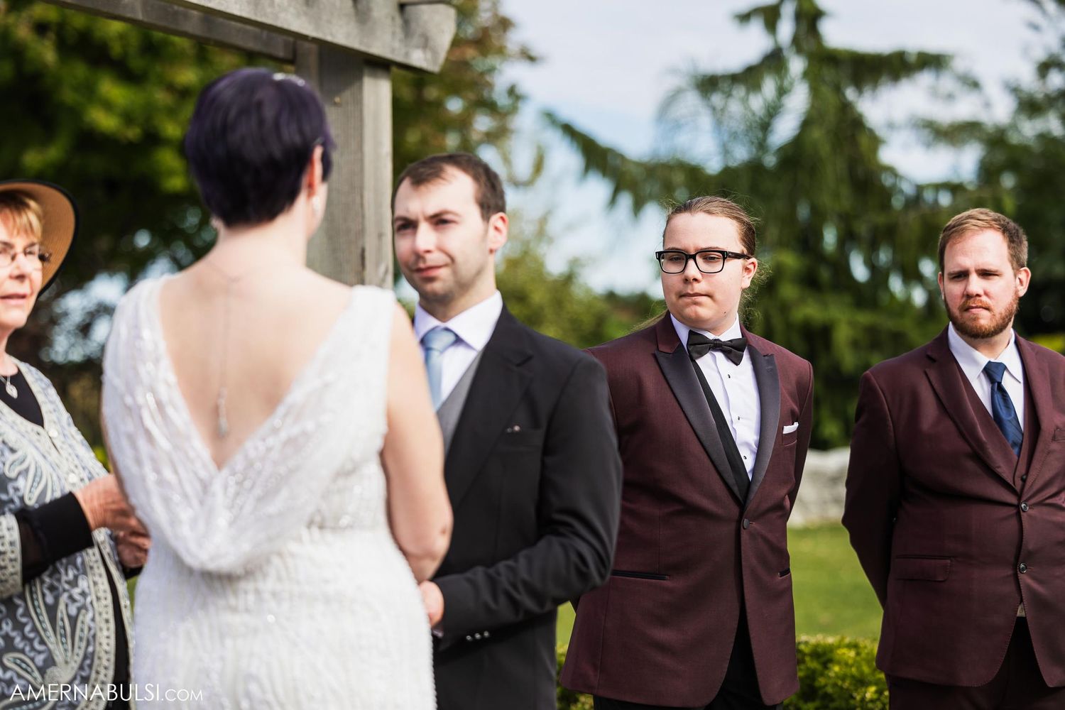 Wedding ceremony under evergreen trees with wedding party members in formal attire.