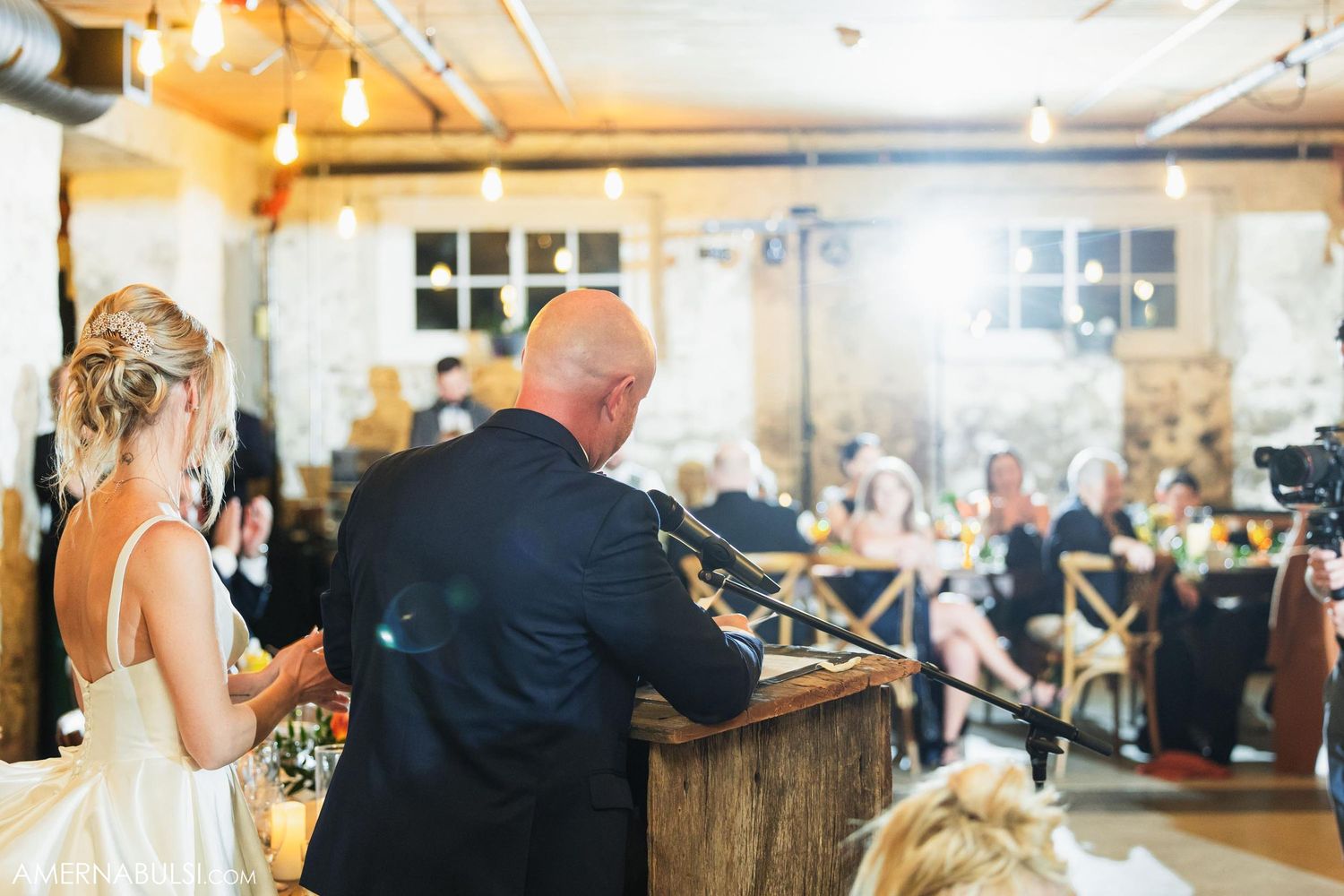 A couple gives a speech from behind a wooden podium at their wedding reception.