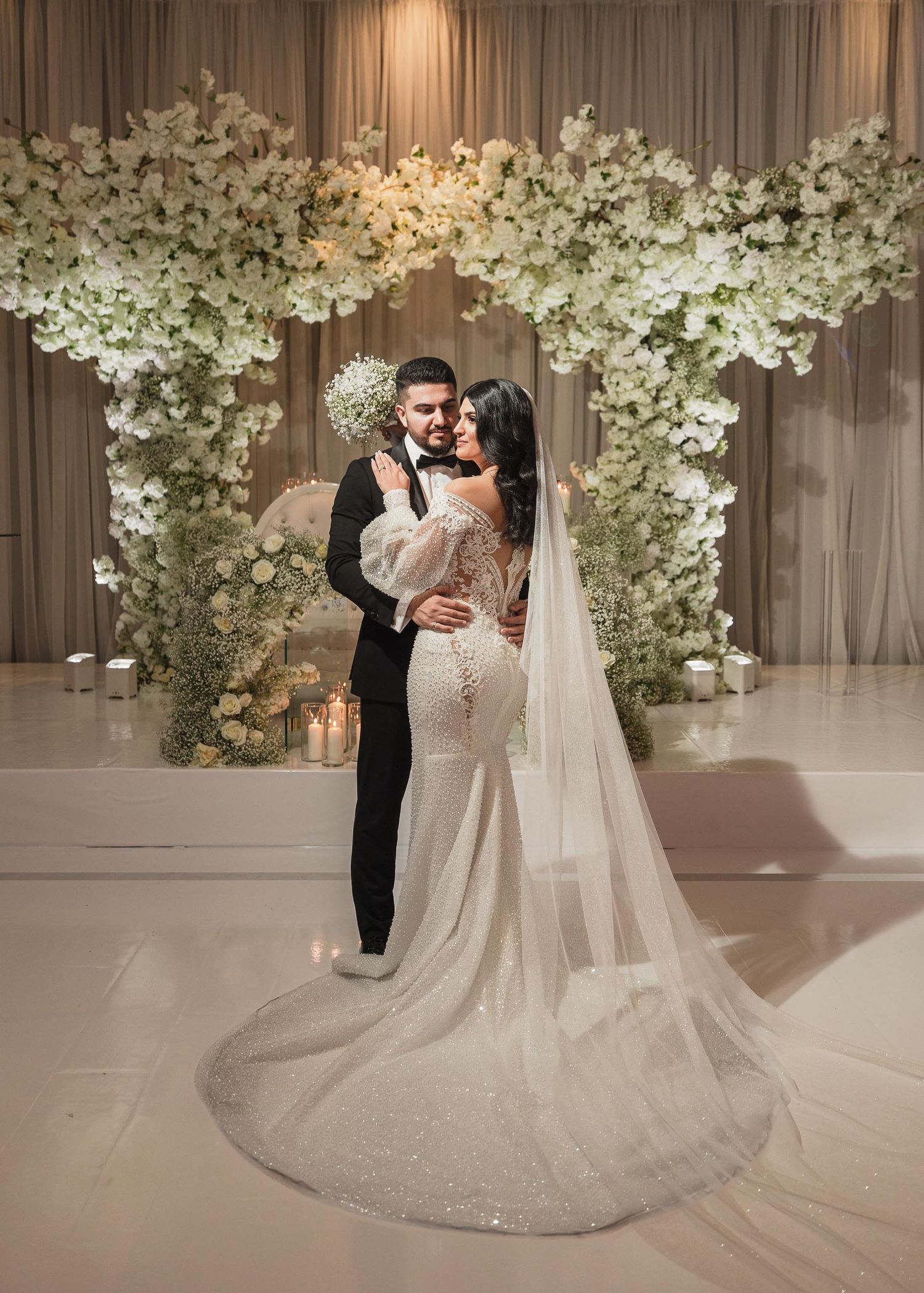 Wedding ceremony setup with luxurious white floral arch and elegant couple in formal attire.