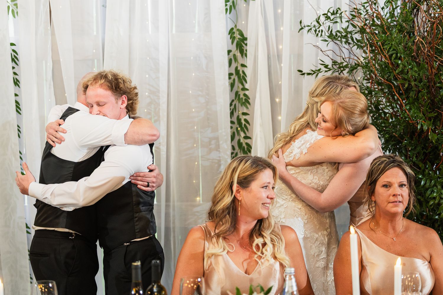 Wedding reception guests laughing together at elegant head table with white floral decorations.