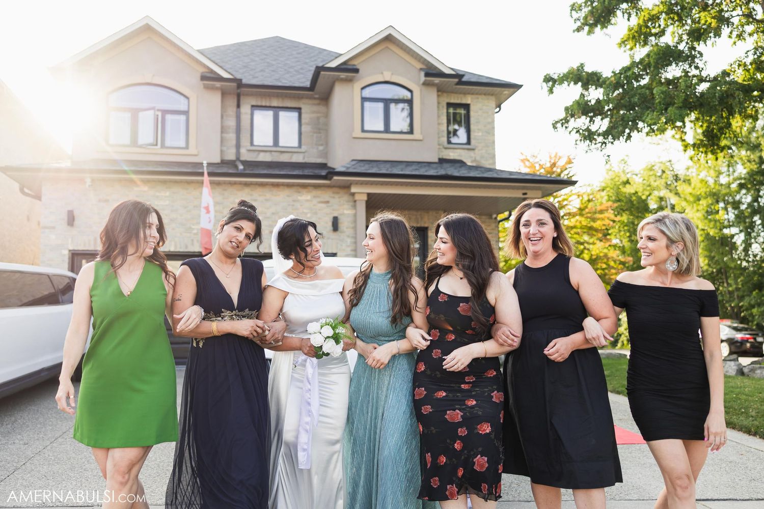 Group gathering outside a large house in colorful dresses during sunset.