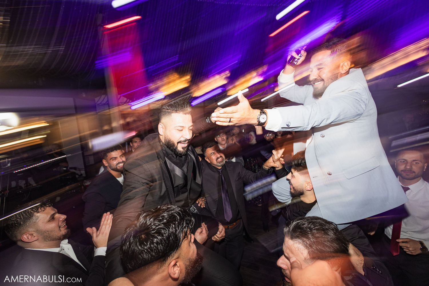A crowded nightclub scene with people dancing and partying under purple and white lighting effects.