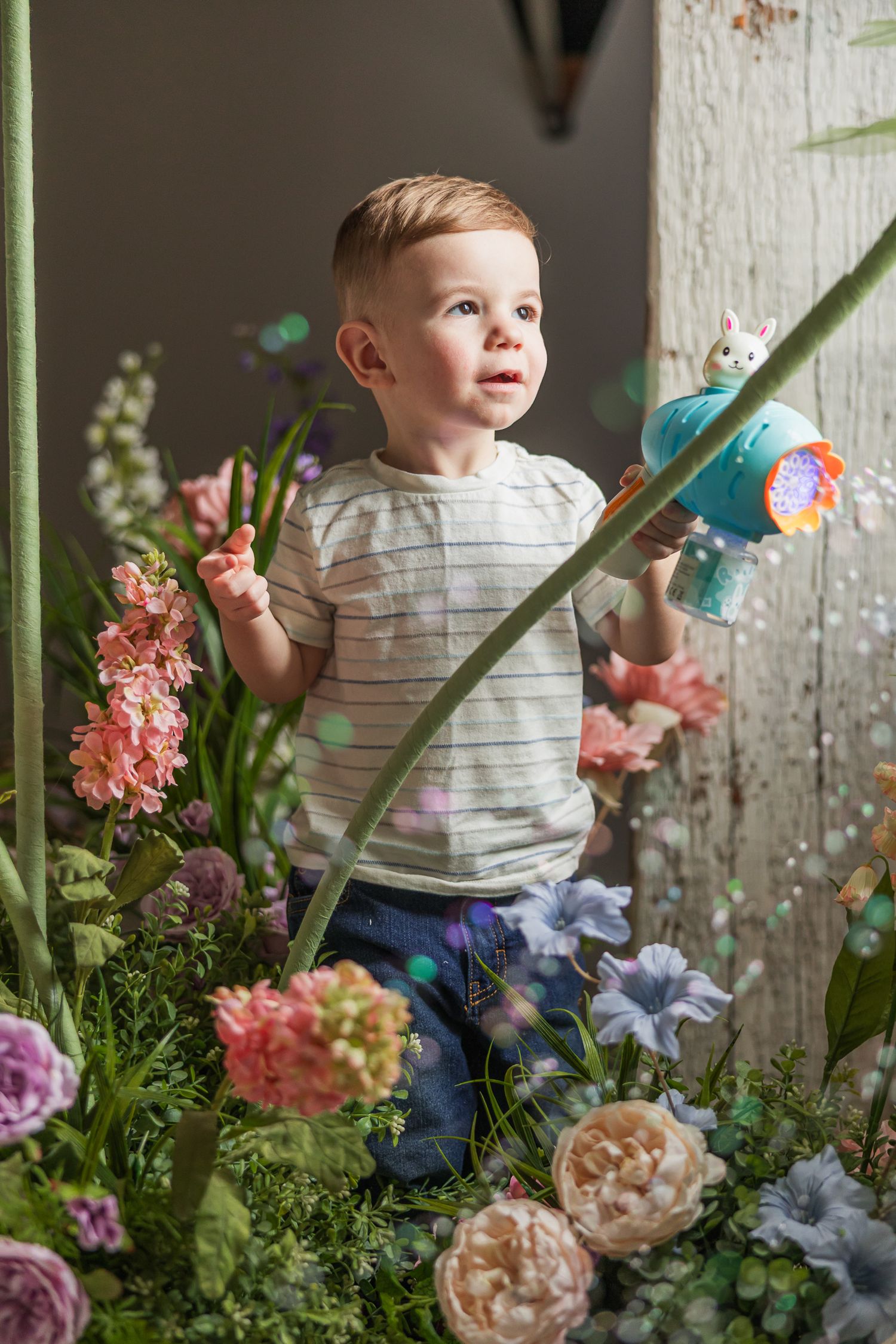 A child plays with bubbles among pink and blue flowers in a rustic garden setting.