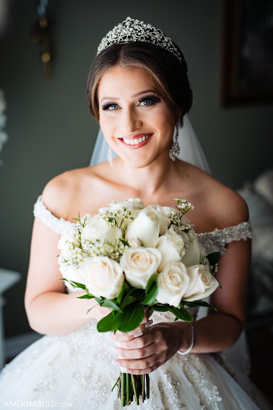 Close-up of a white bridal bouquet with roses and delicate details against a wedding dress.