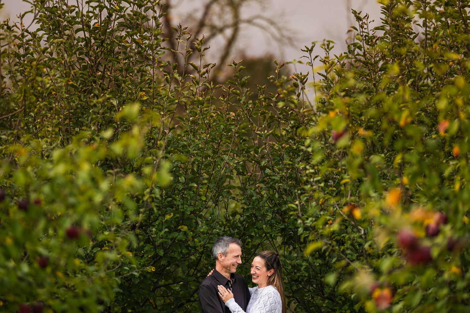 A couple shares an intimate moment surrounded by lush greenery in an outdoor garden setting.