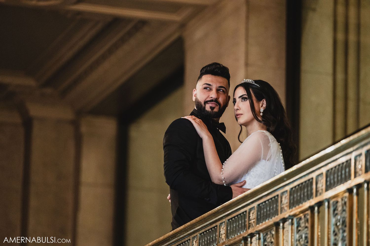Romantic couple embraces on an elegant staircase in a historic building with ornate architectural details.