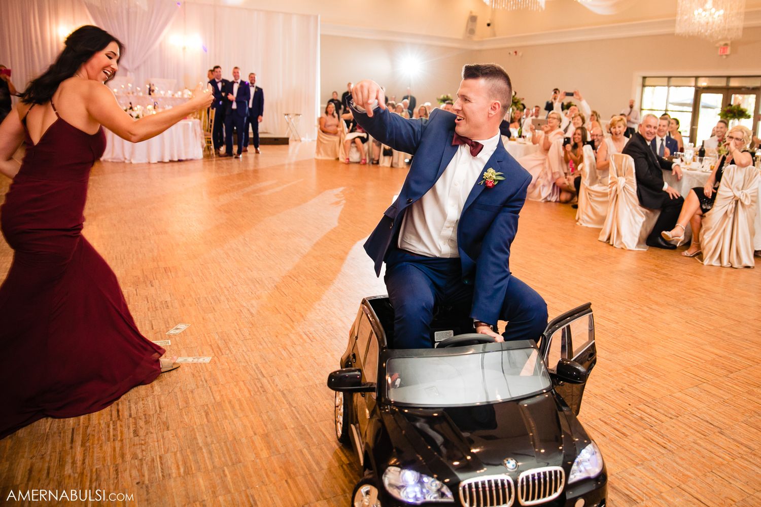 People dancing and celebrating at an elegant wedding reception in a grand ballroom with warm lighting and wooden floors.