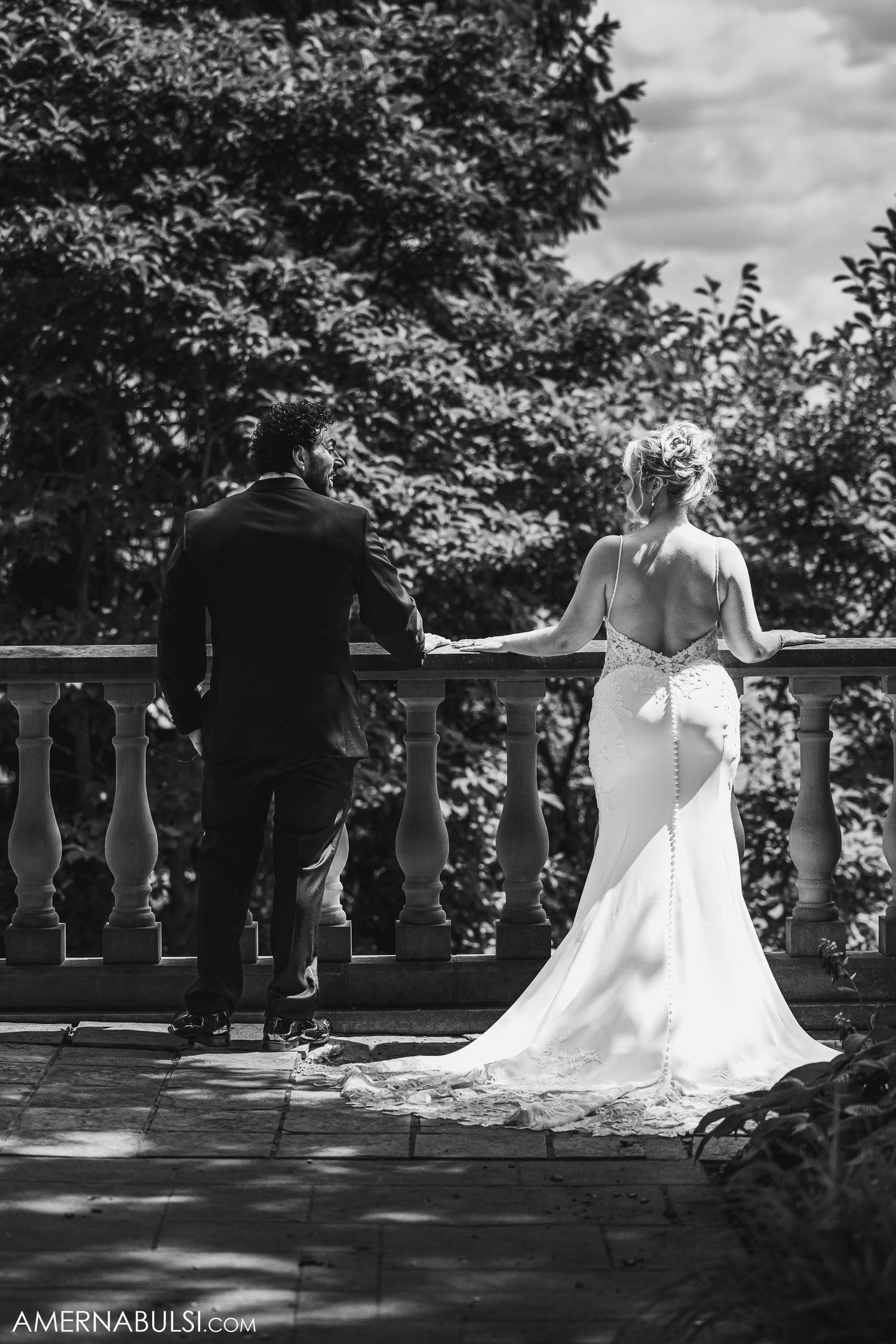 Black and white photo of couple standing at stone balustrade overlooking garden landscape.