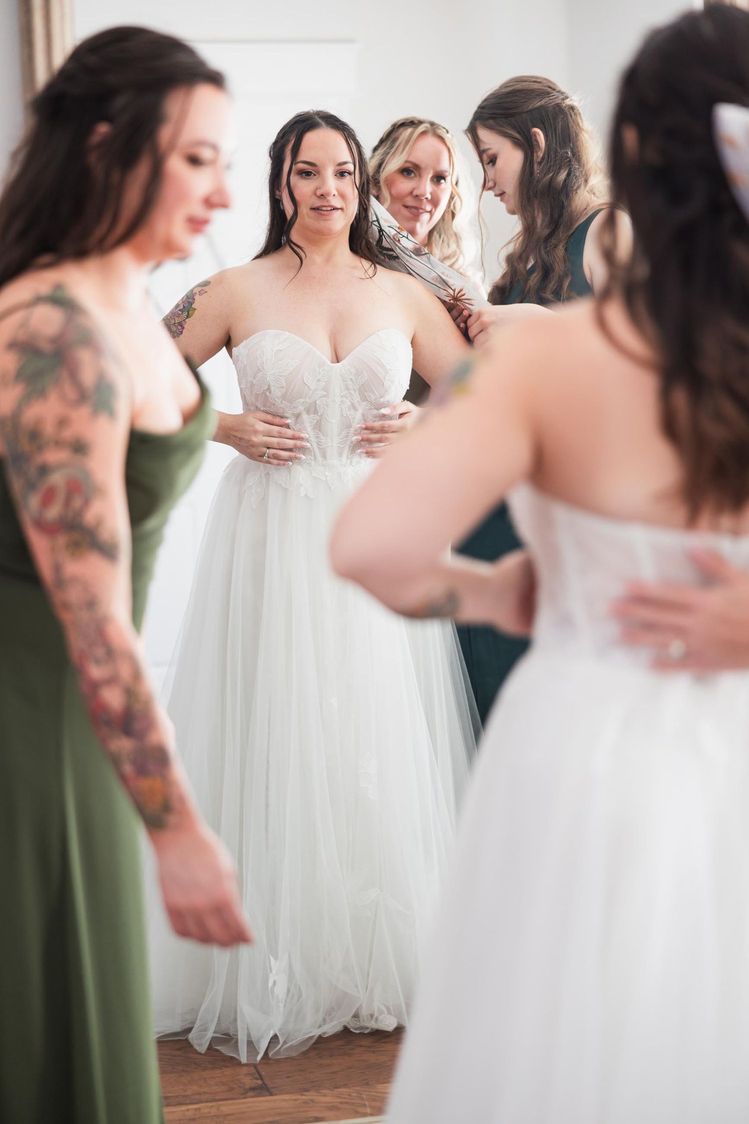 Wedding dress fitting moment with bridesmaids in sage green dresses.