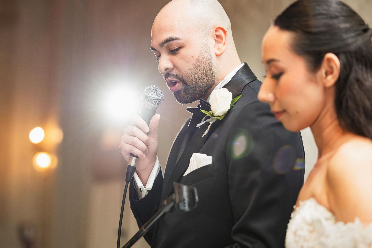 Couple speaks into microphone during emotional wedding reception moment.