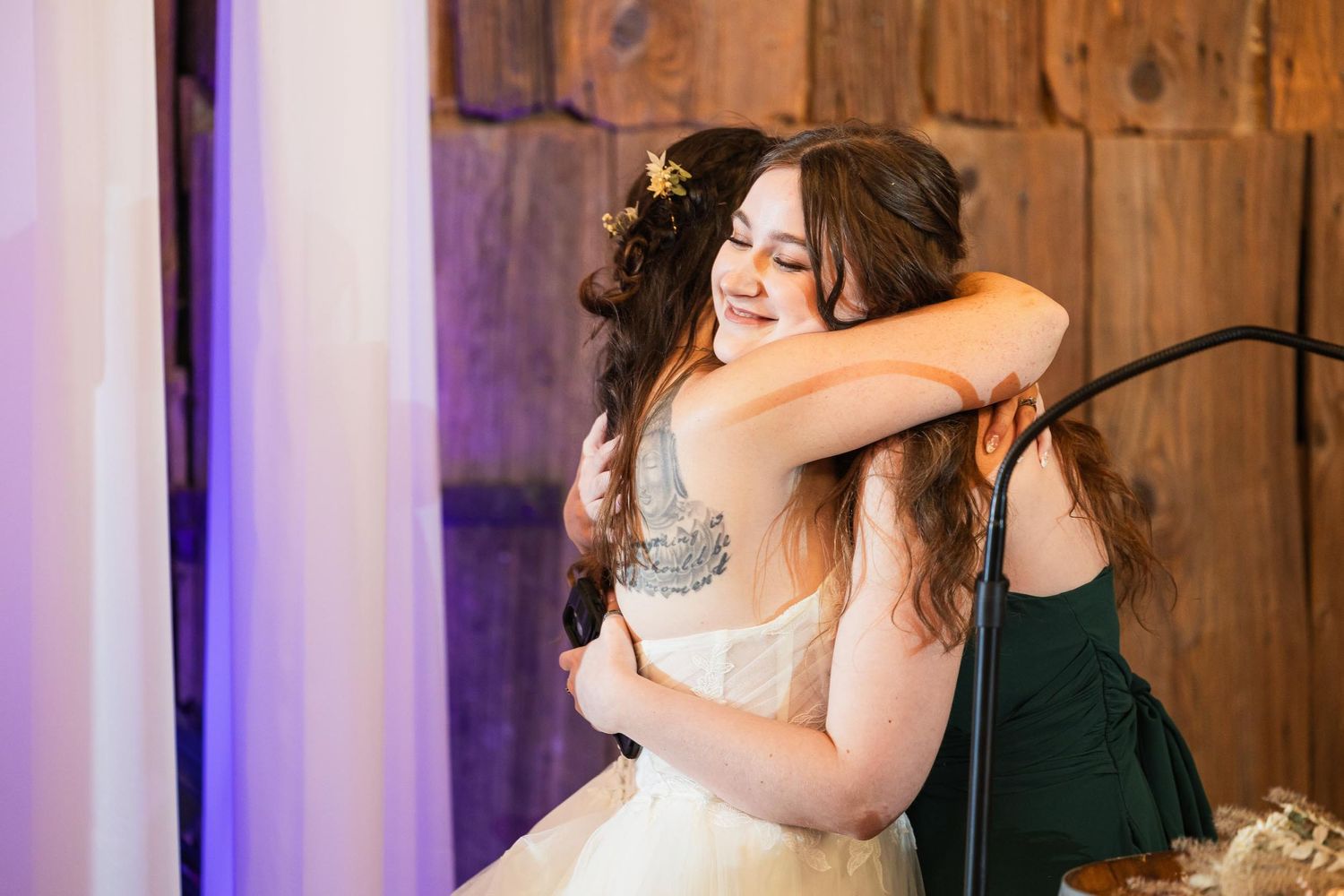 An emotional embrace during a wedding reception in a rustic wooden venue with purple lighting.