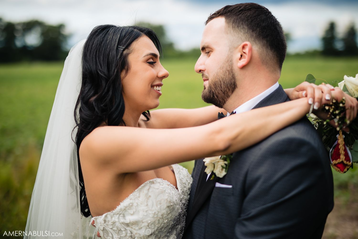 A romantic wedding portrait of a couple embracing in a green field on their special day.