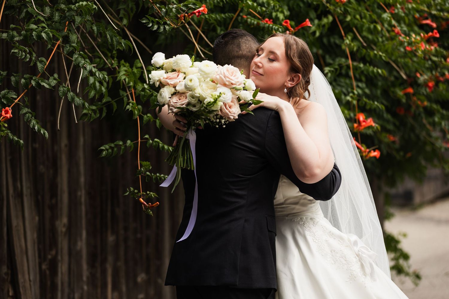 Newlyweds share a romantic kiss beside a wall of green vines, bride holding a white floral bouquet.