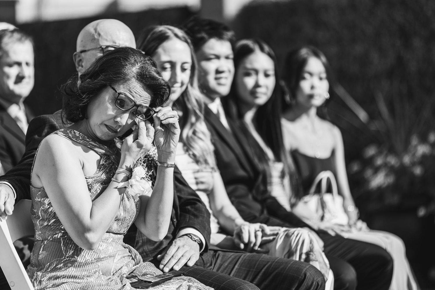 Emotional wedding guest wiping tears during outdoor ceremony, captured in black and white photography.
