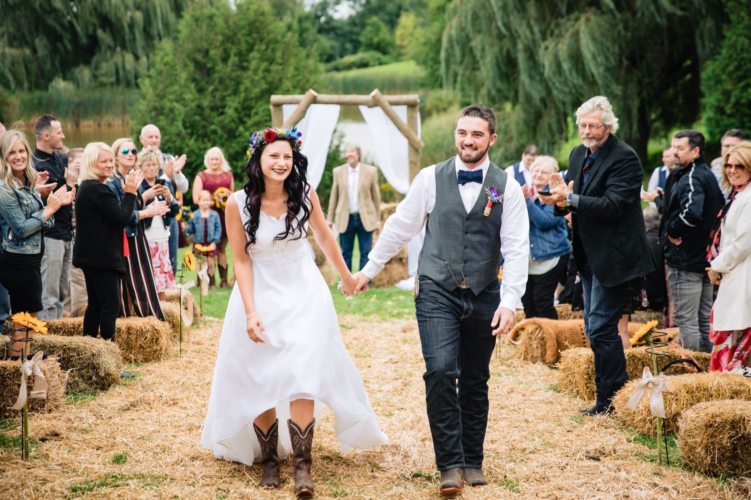 Wedding party walks through a rustic outdoor setting with hay bales and natural scenery.