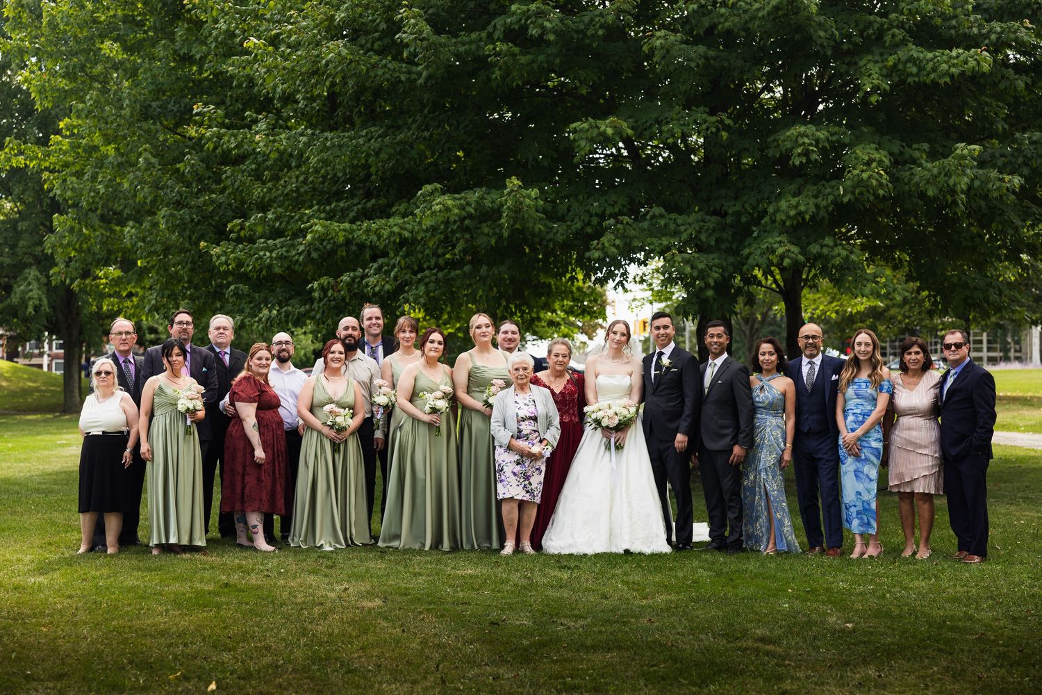 Large wedding family group portrait on green lawn with trees in background.