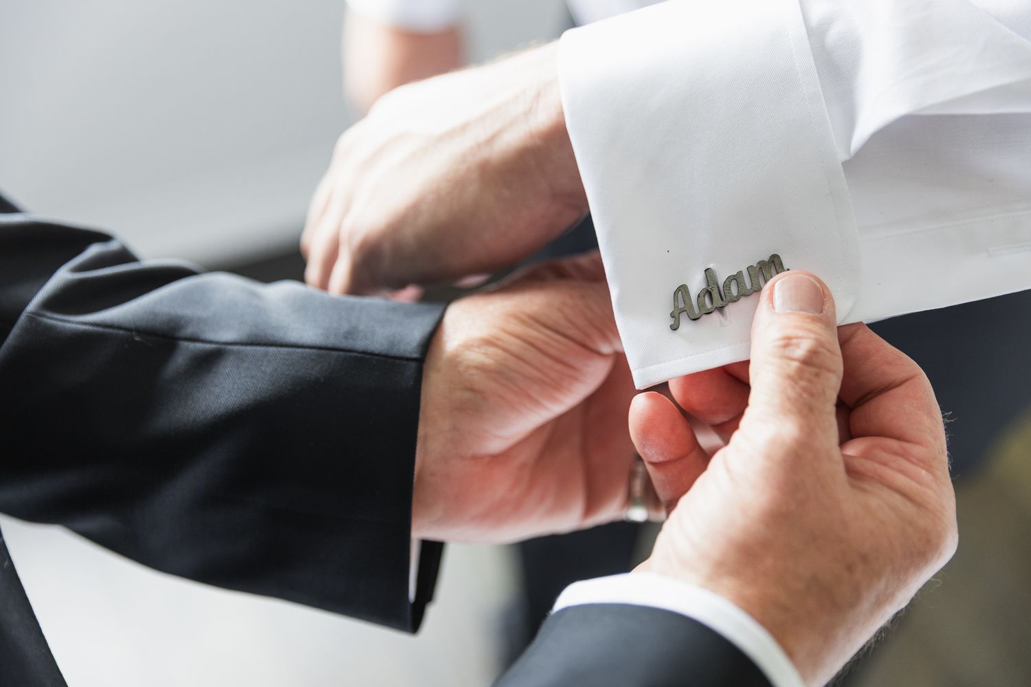 Close-up of personalized cufflinks engraved with name Adam on groom wedding suit sleeve.