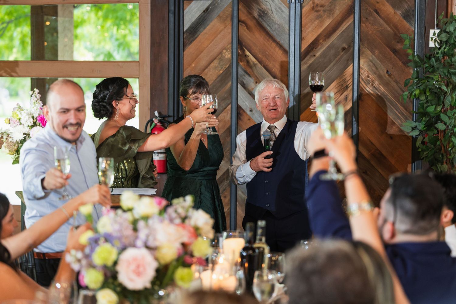 Wedding guests raise glasses in a joyful toast during the reception inside a rustic barn venue.