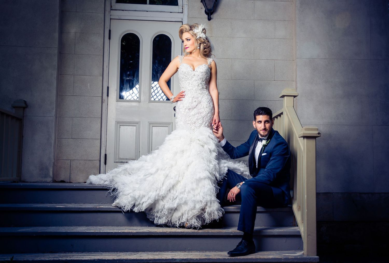 Dramatic wedding portrait on stone steps featuring ornate white dress and classic architecture.