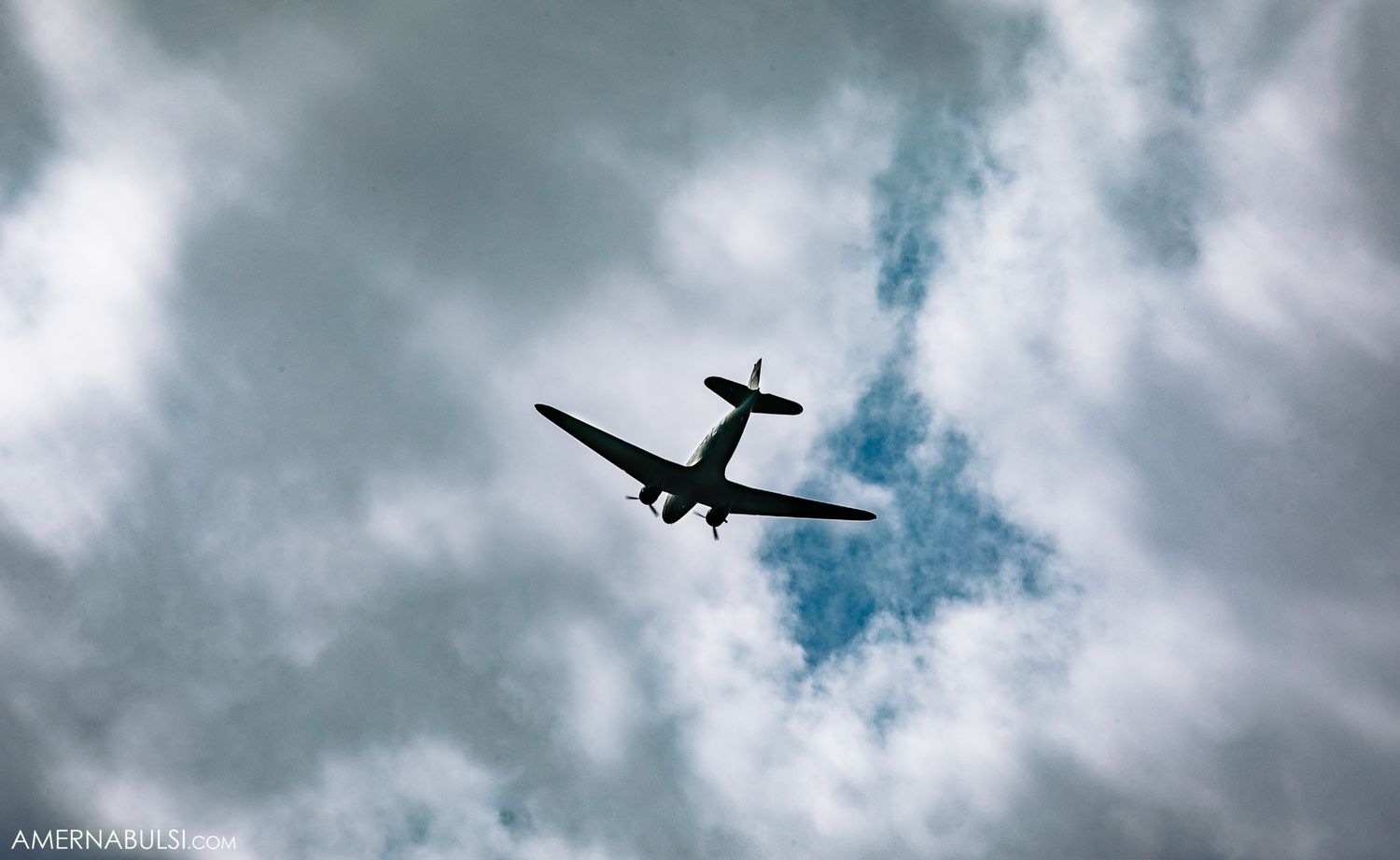 Silhouette of small airplane flying against dramatic cloudy sky.