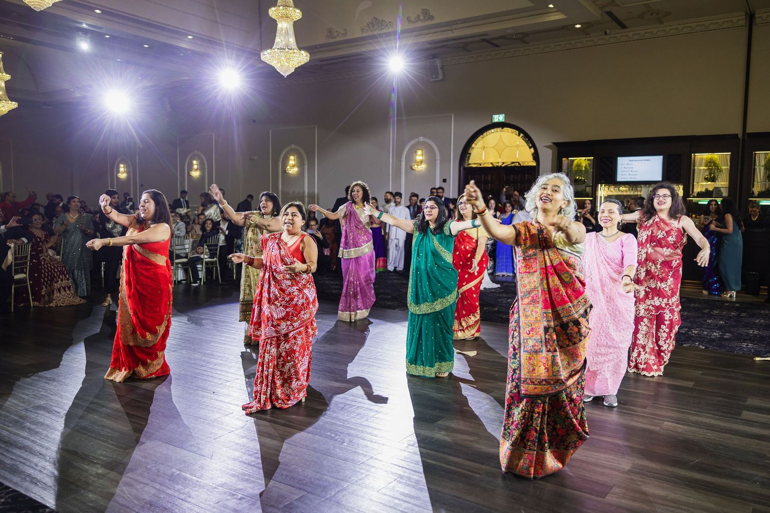 Group of dancers performing traditional Indian dance moves in colorful saris under stage lighting.