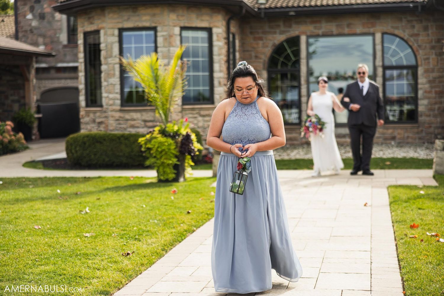 Bridesmaid in powder blue dress holding bouquet on mansion lawn during wedding.