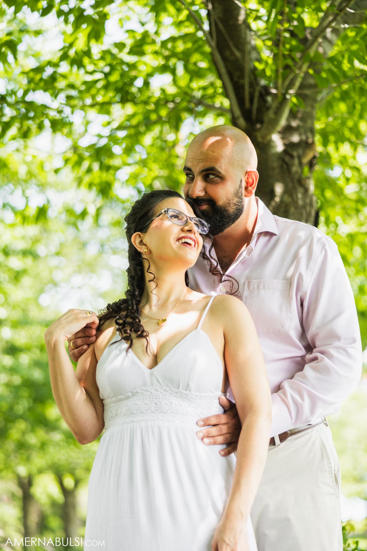 Couple sharing laughter under green leafy trees in summer.