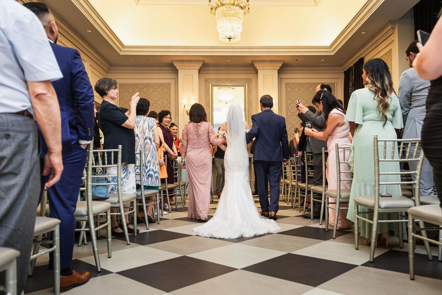 Wedding ceremony in elegant ballroom with checkered floor and Chiavari chairs.