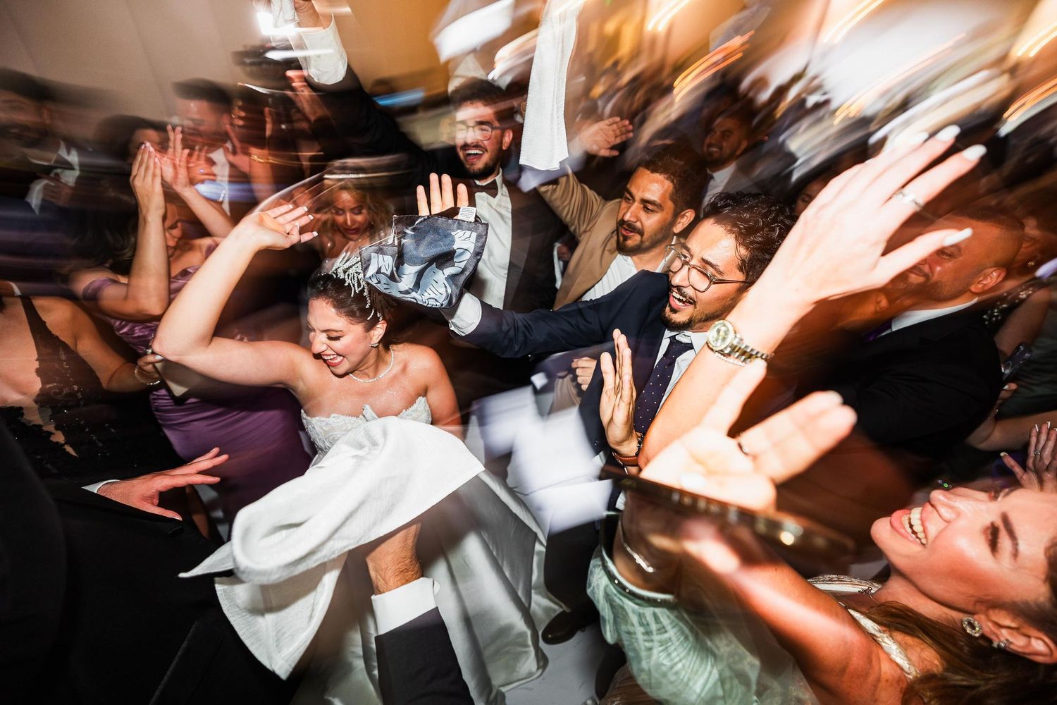 Motion-blurred shot of wedding celebration with guests dancing enthusiastically.