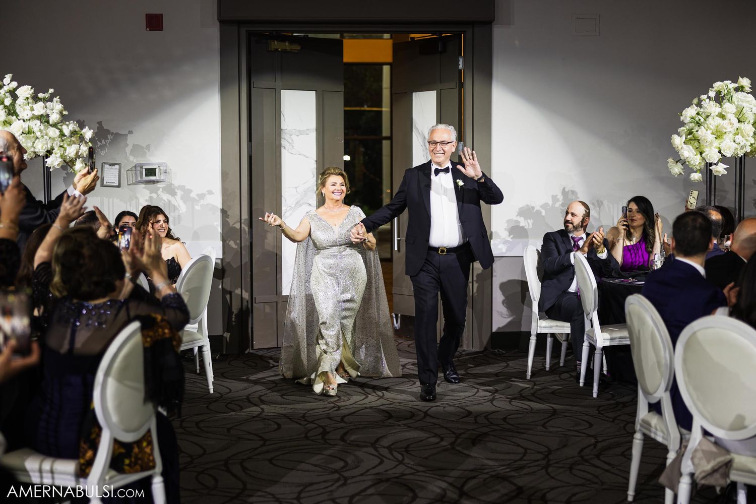 Celebratory entrance of couple at wedding reception with white floral decorations and cheering guests.