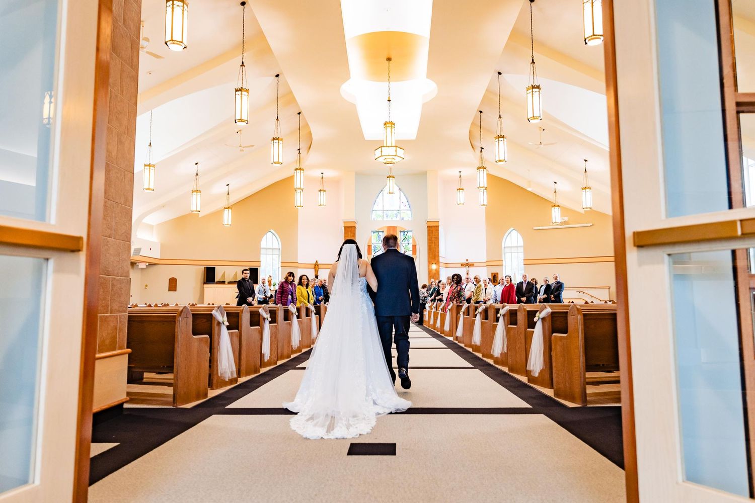 A couple walking down the church aisle after their wedding ceremony with elegant lighting overhead.