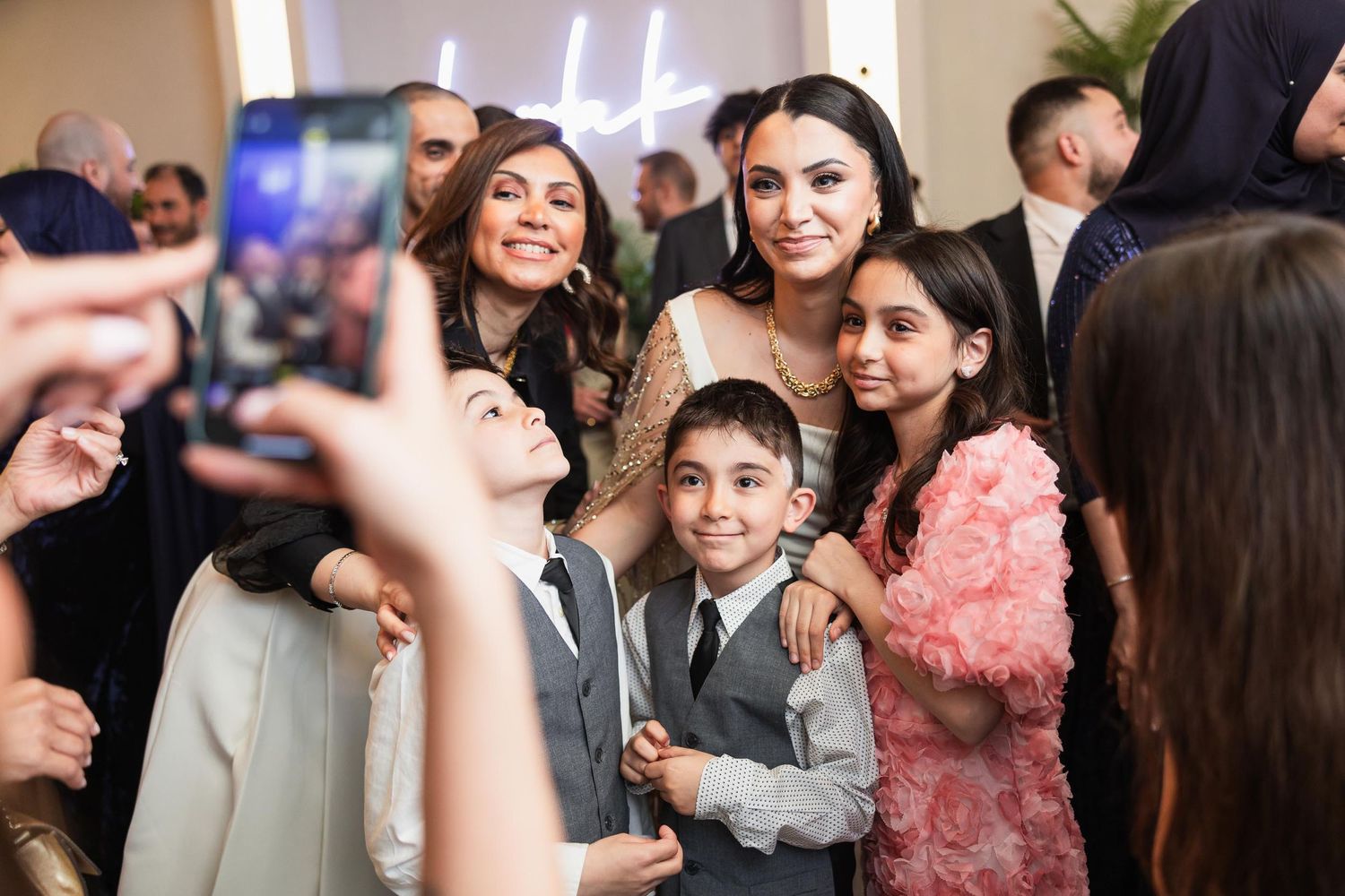 Joyful wedding celebration with guests taking photos on smartphones.