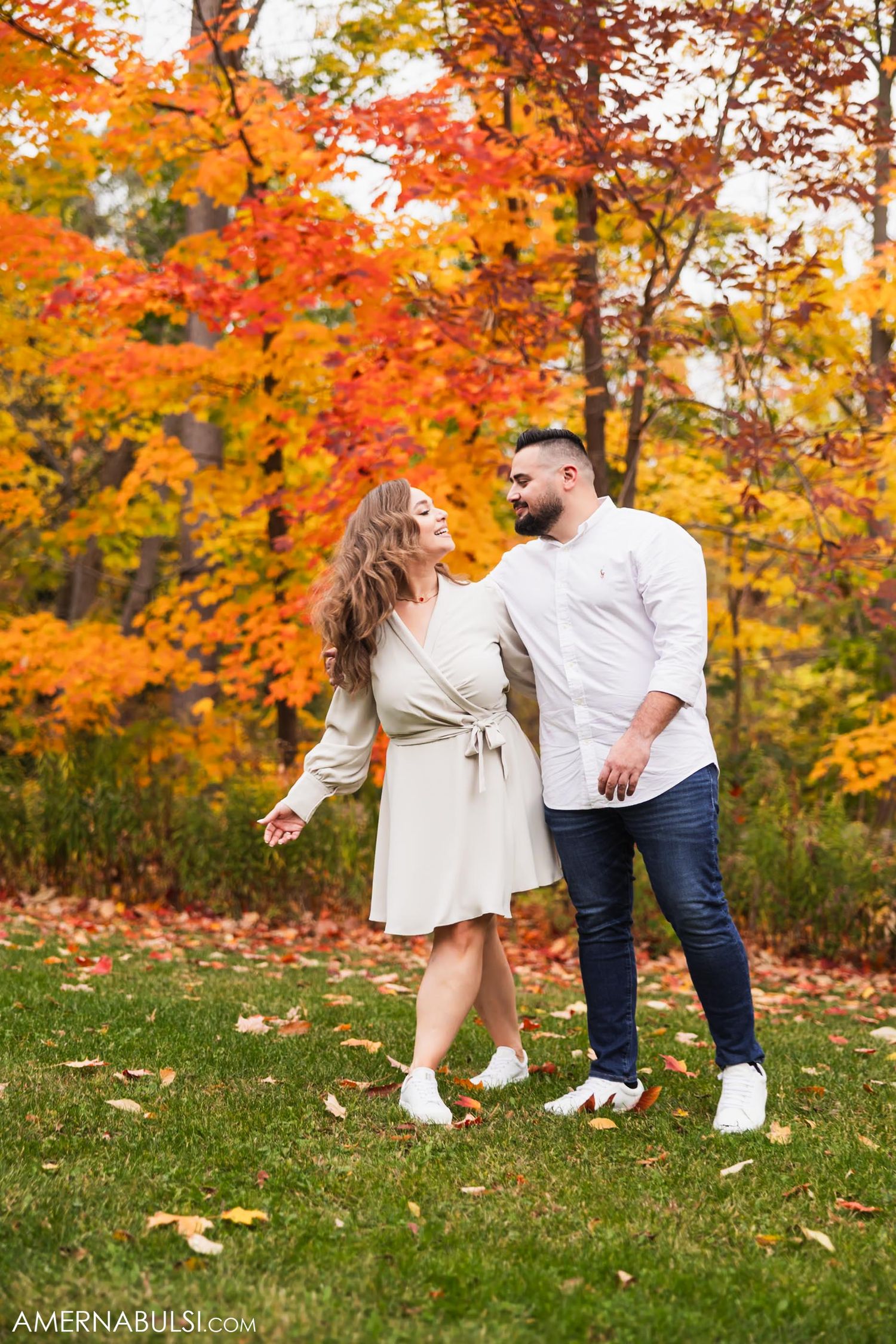 A romantic autumn engagement photo with vibrant orange fall foliage in the background.