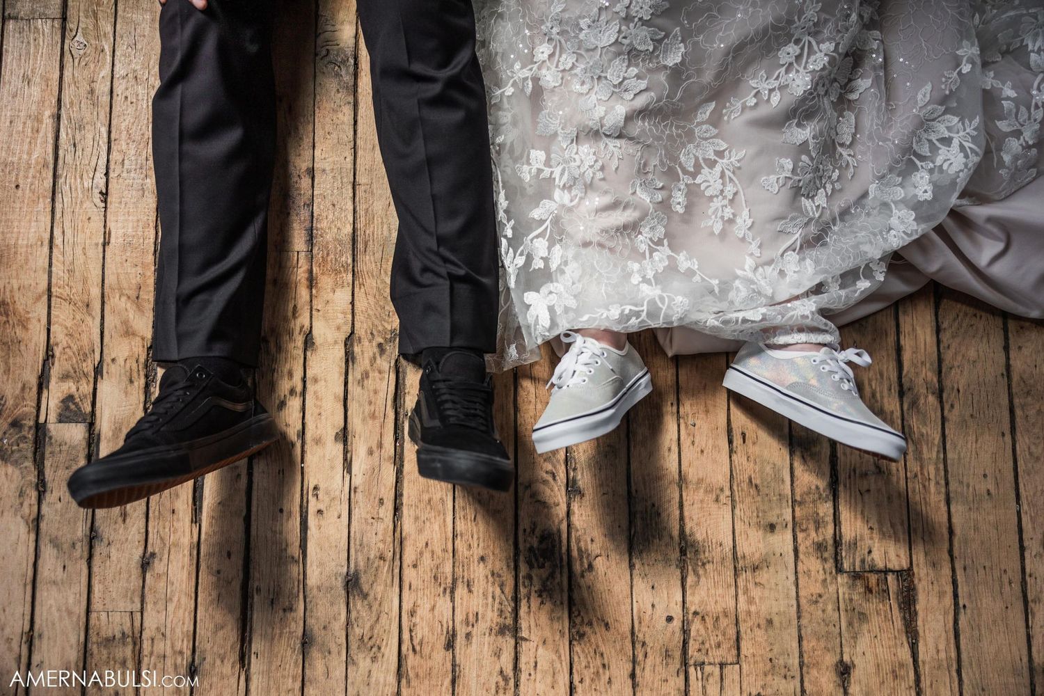Black dress shoes and white sneakers on rustic wooden floorboards at a wedding.