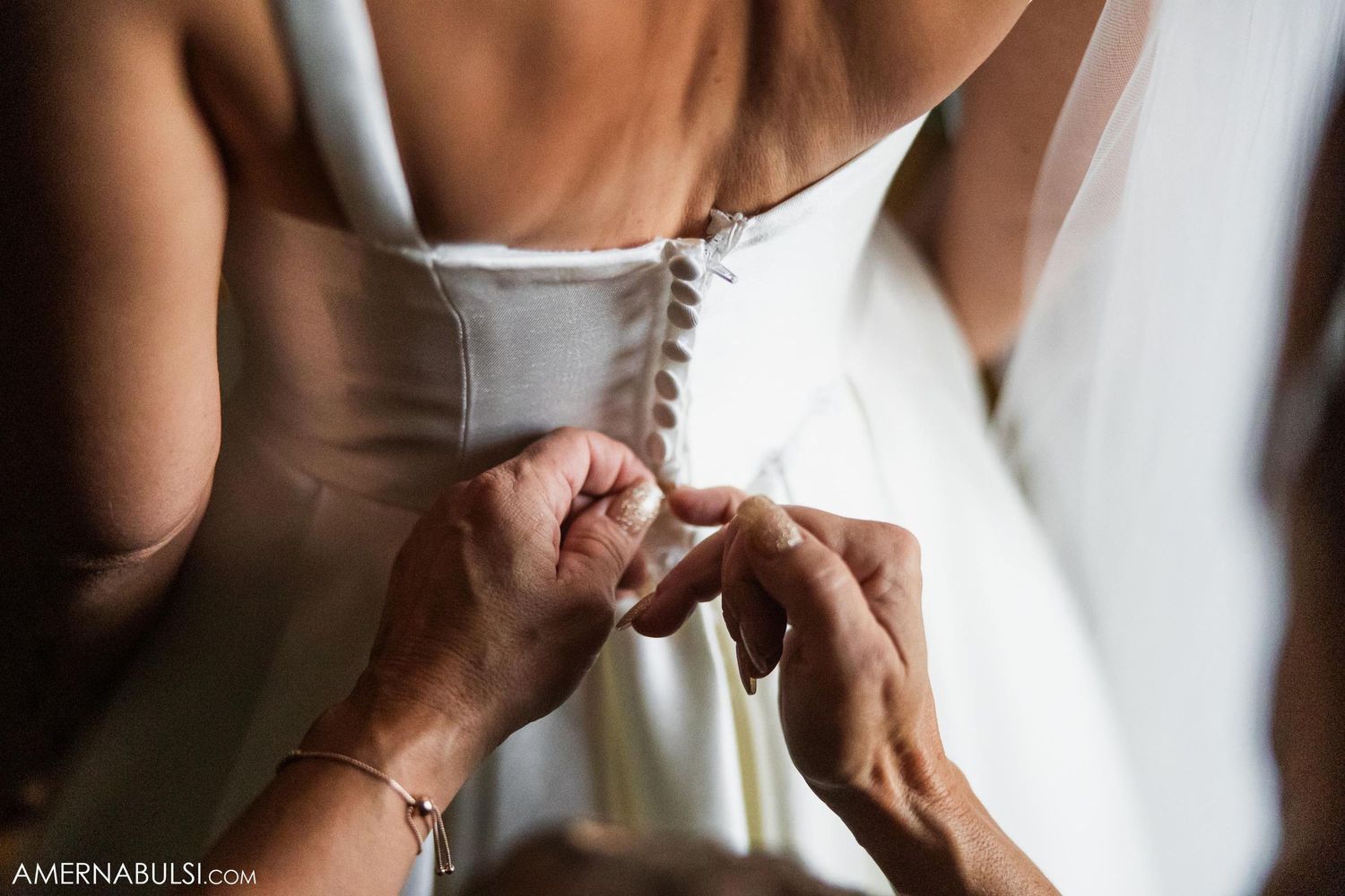 Close-up detail shot of hands fastening buttons on back of white wedding dress.