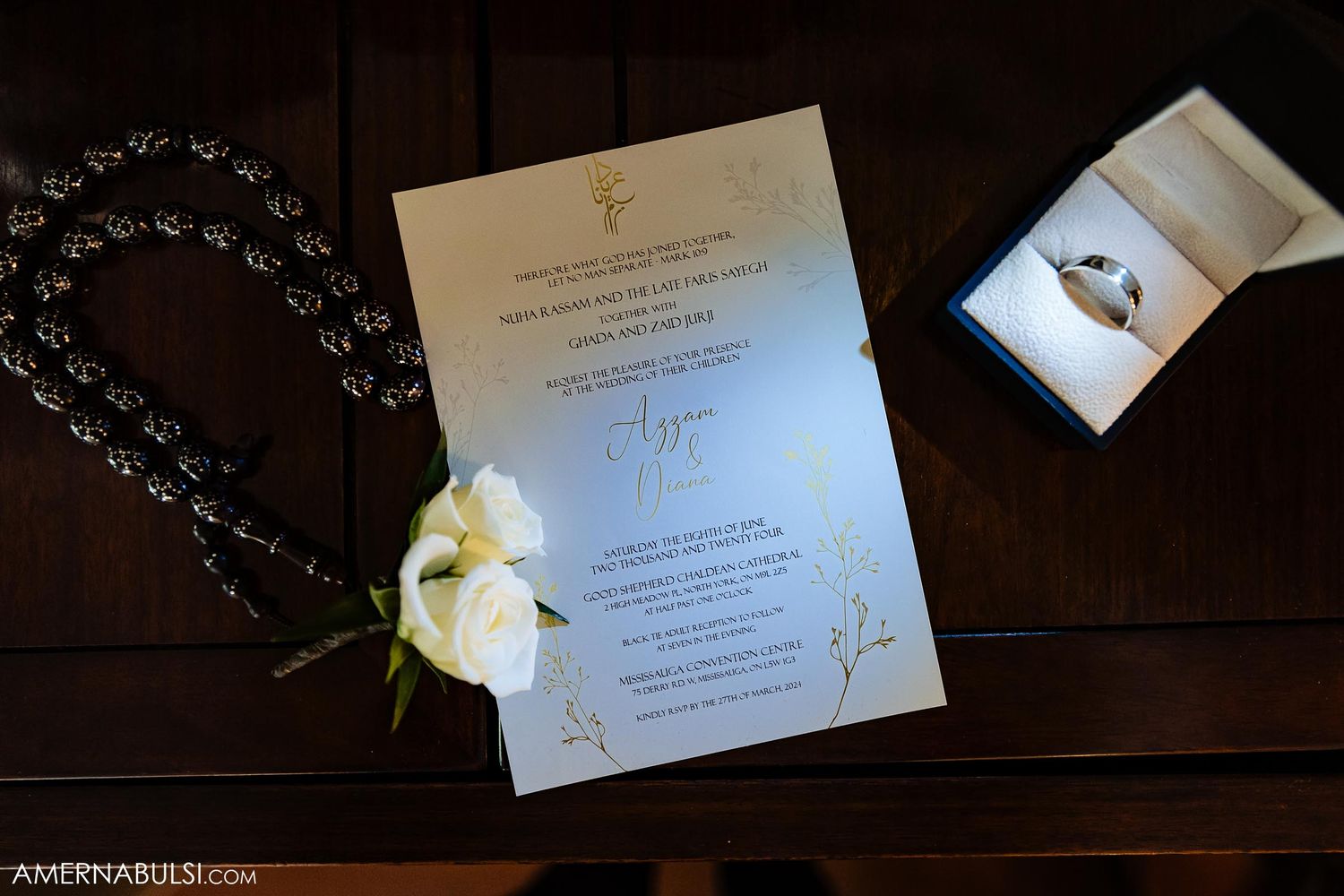 Wedding invitation and white orchid flower laid on dark wooden surface with decorative beads.
