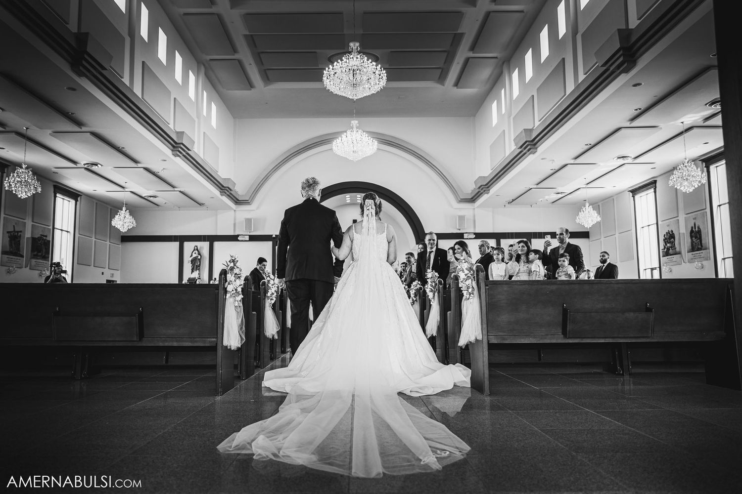 Black and white photo of wedding ceremony in church with chandelier and arched ceiling.