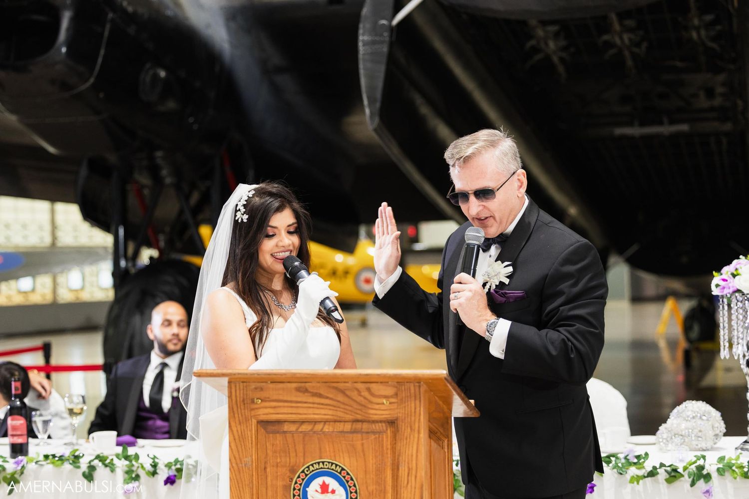 Wedding ceremony taking place in aircraft hangar with podium and floral decorations.