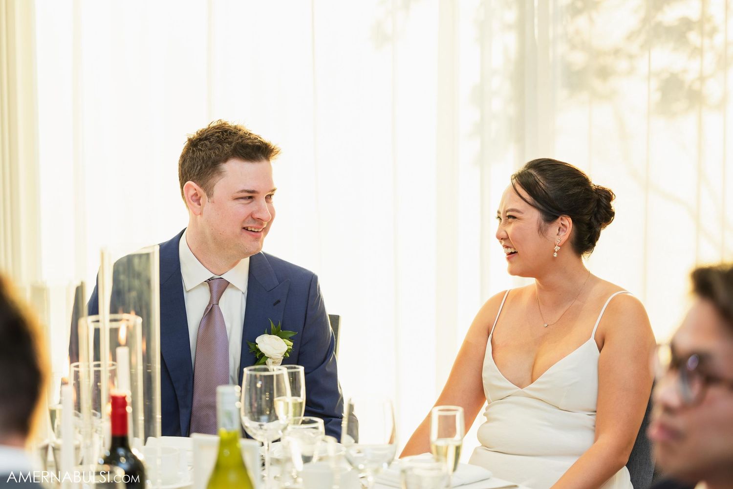 A couple shares a candid laughing moment at their wedding reception table.