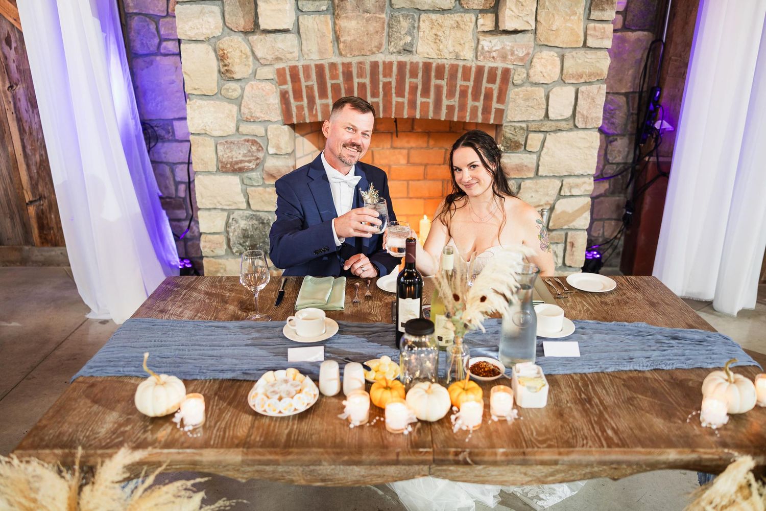 A couple toasts at their sweetheart table decorated with pumpkins and autumn decor.