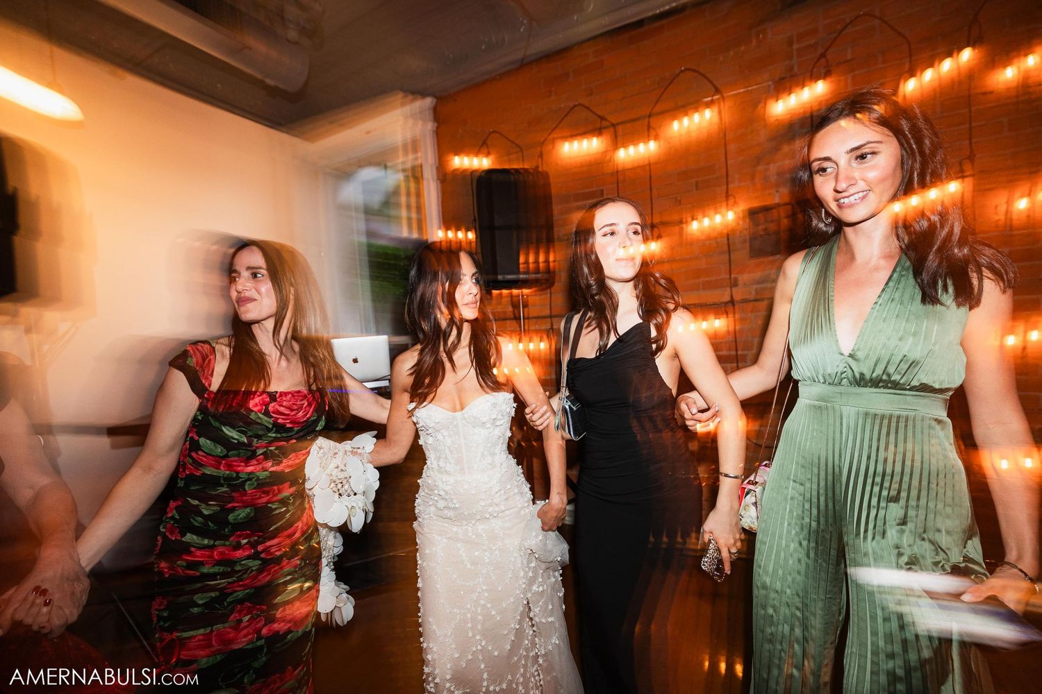 Motion-blurred dancing scene at wedding reception with string lights.